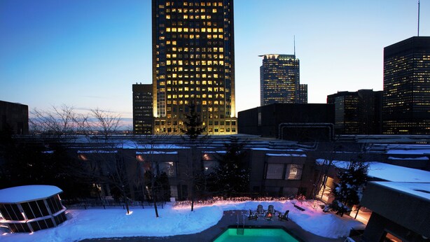 A swimming pool surrounded by snow with people swimming, set against a city skyline at dusk. - Hotel Bonaventure Montreal (Montreal)