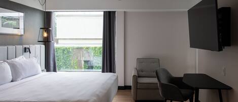 Una habitación de hotel moderna con una cama grande, un escritorio, una silla, un televisor y una ventana con cortinas.