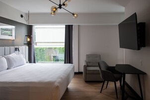 Una habitación de hotel moderna con una cama grande, un escritorio, una silla, un televisor y una ventana con cortinas.