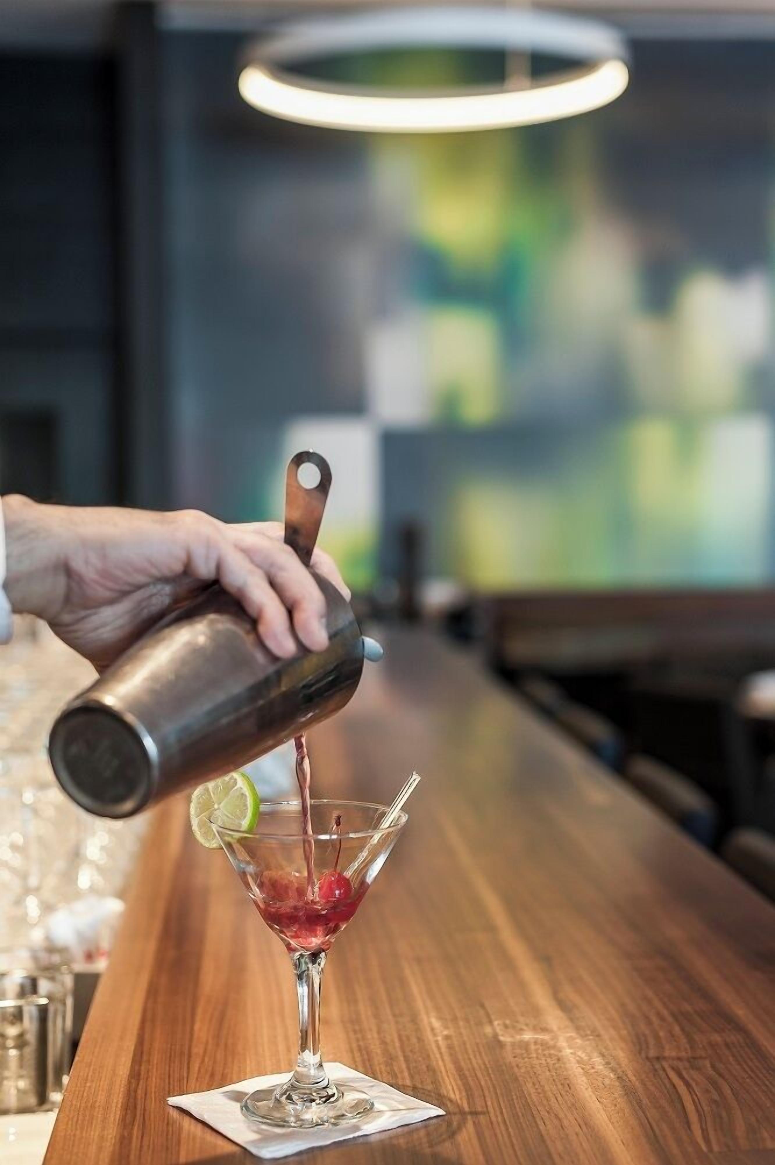 Ein Barkeeper gießt ein Getränk in ein Martini-Glas auf einer Holztresen.