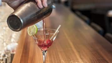Ein Barkeeper gießt ein Getränk in ein Martini-Glas auf einer Holztresen.