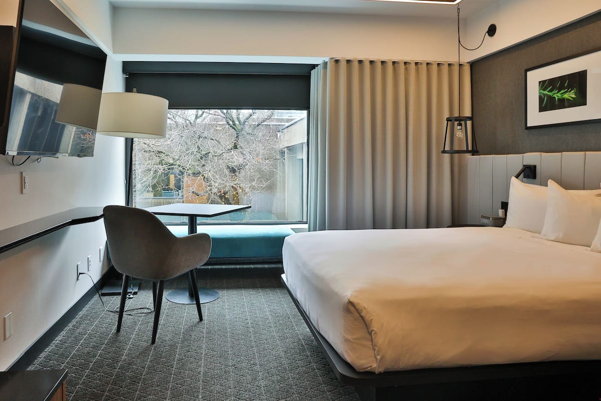 A hotel room with a bed, a desk, a chair, a TV, and a window with curtains.