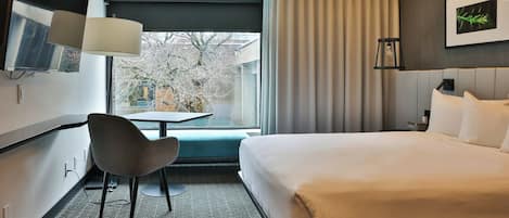 A hotel room with a bed, a desk, a chair, a TV, and a window with curtains.