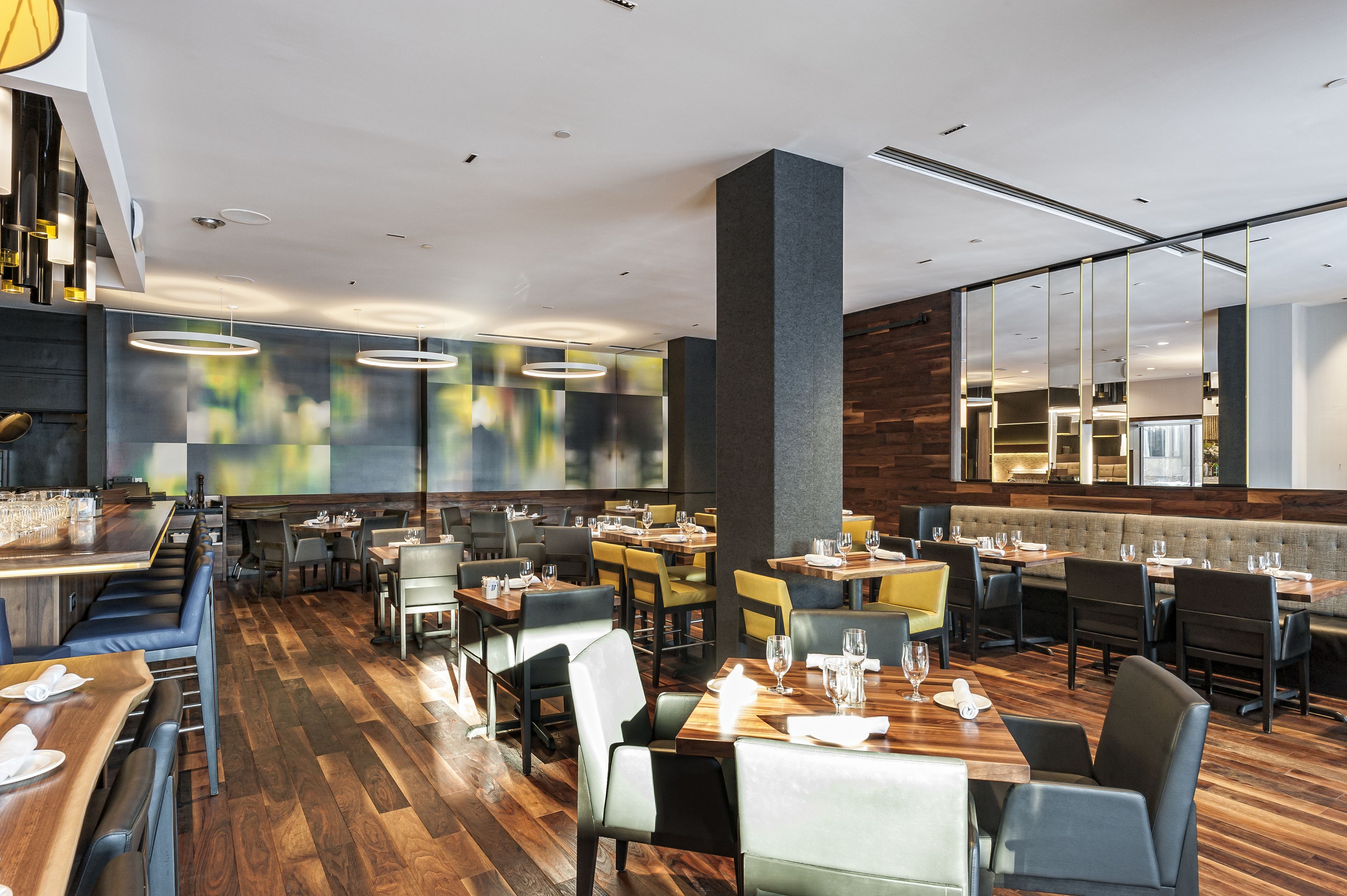 Ein modernes Restaurant mit Holzböden, verschiedenen Essbereichen und zeitgemäßer Beleuchtung.