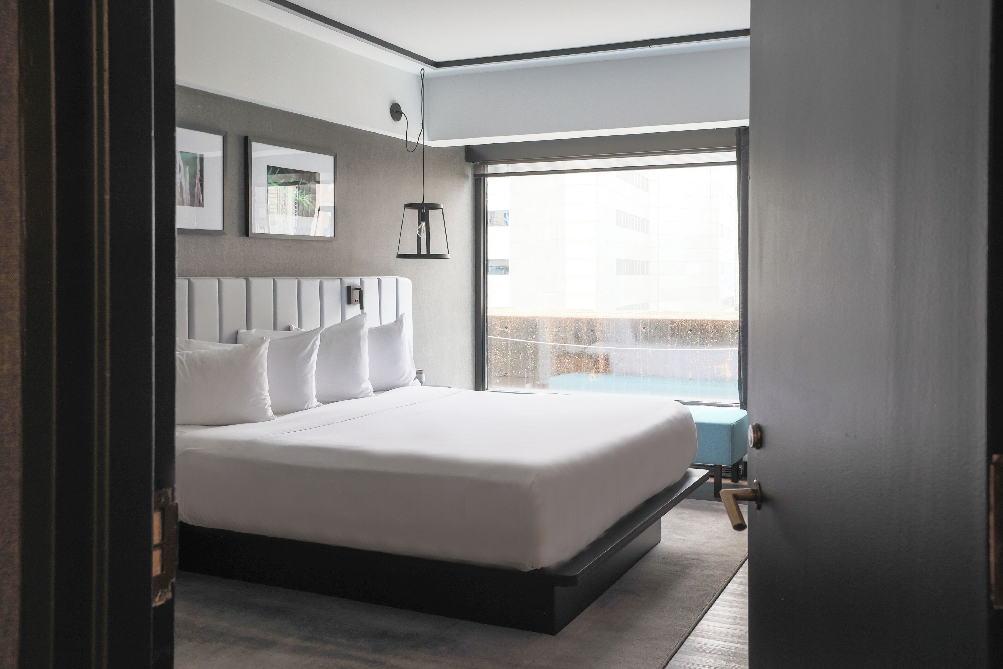 A modern bedroom with a large bed, a view of the city, and a small window.