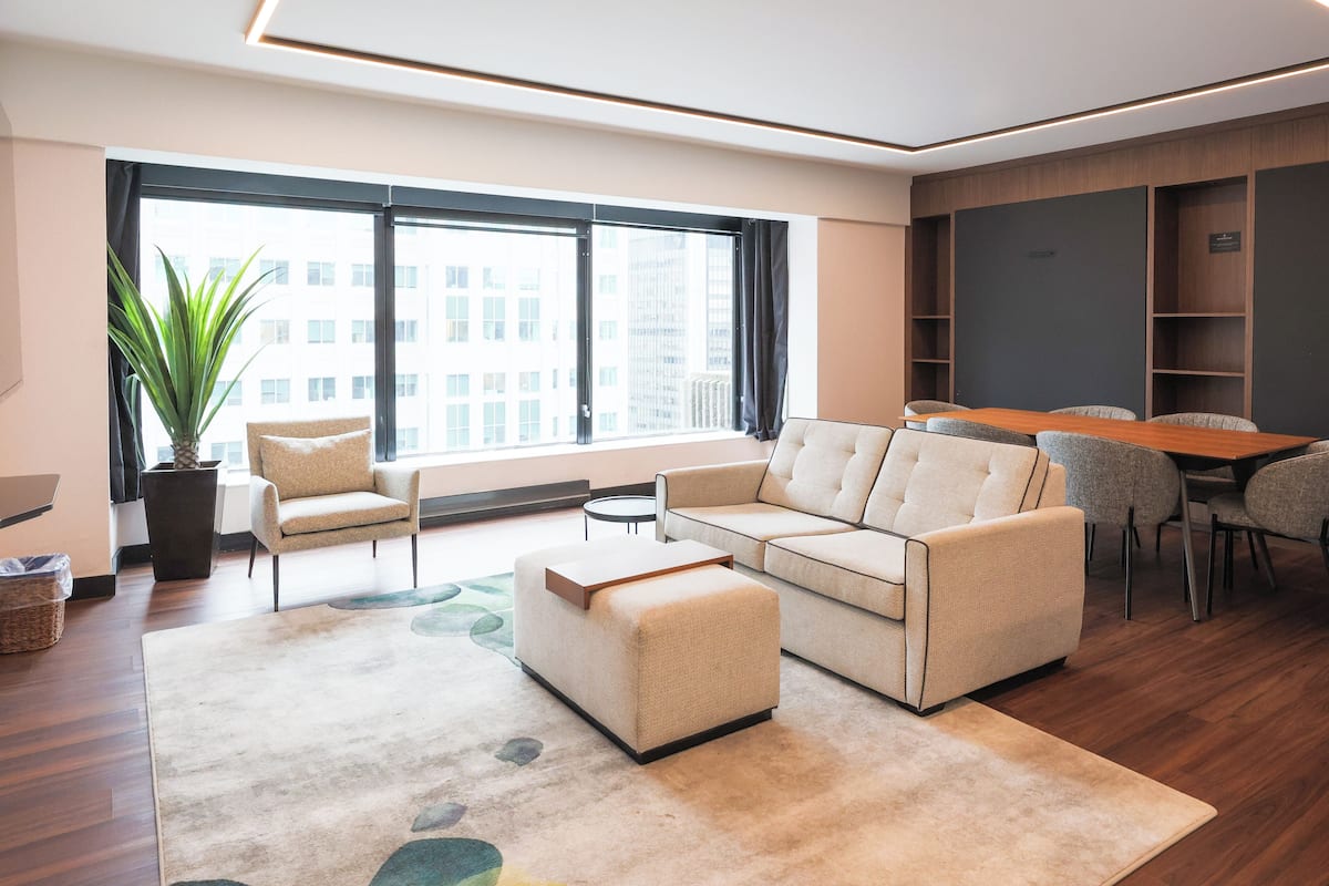 A modern living room with a sofa, armchairs, a coffee table, and a dining area with chairs.