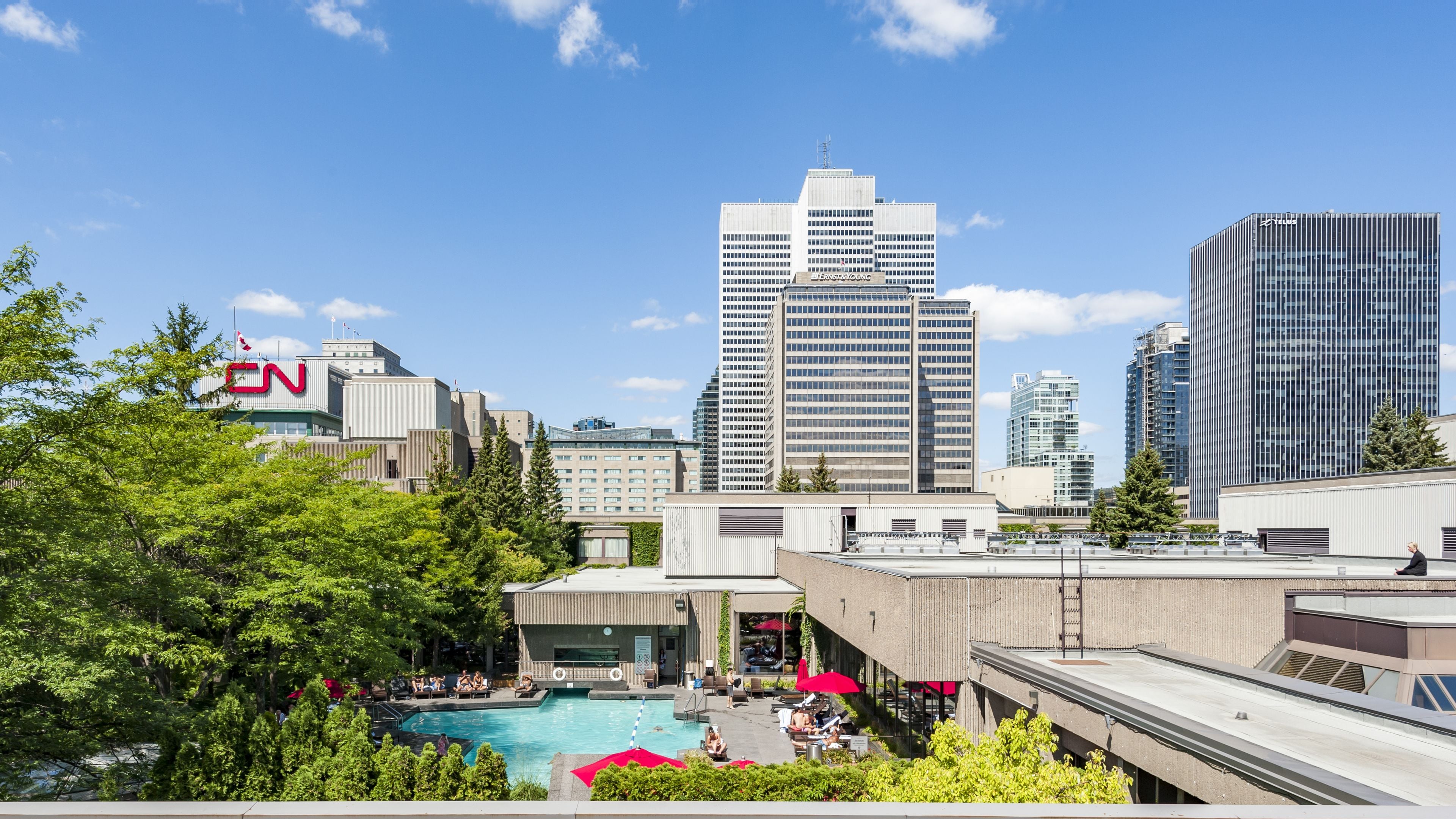 A modern hotel with a rooftop pool, surrounded by urban skyscrapers and lush greenery.