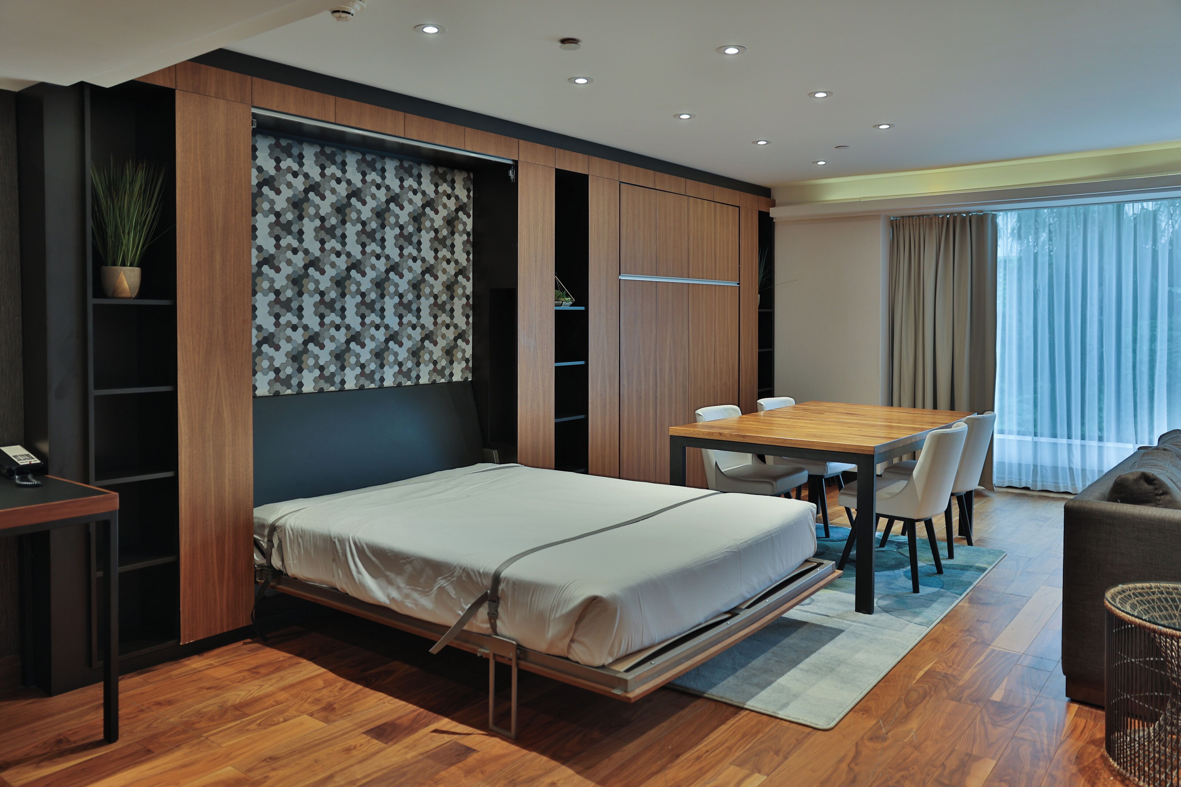 Un dormitorio moderno con una cama plegable, una mesa de comedor con sillas, un sofá y un amplio ventanal con cortinas.