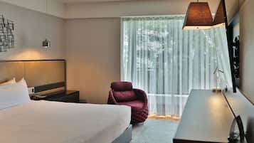 Une chambre d’hôtel moderne, dotée d’un grand lit, d’un bureau, d’une chaise et d’une grande fenêtre avec des rideaux légers.