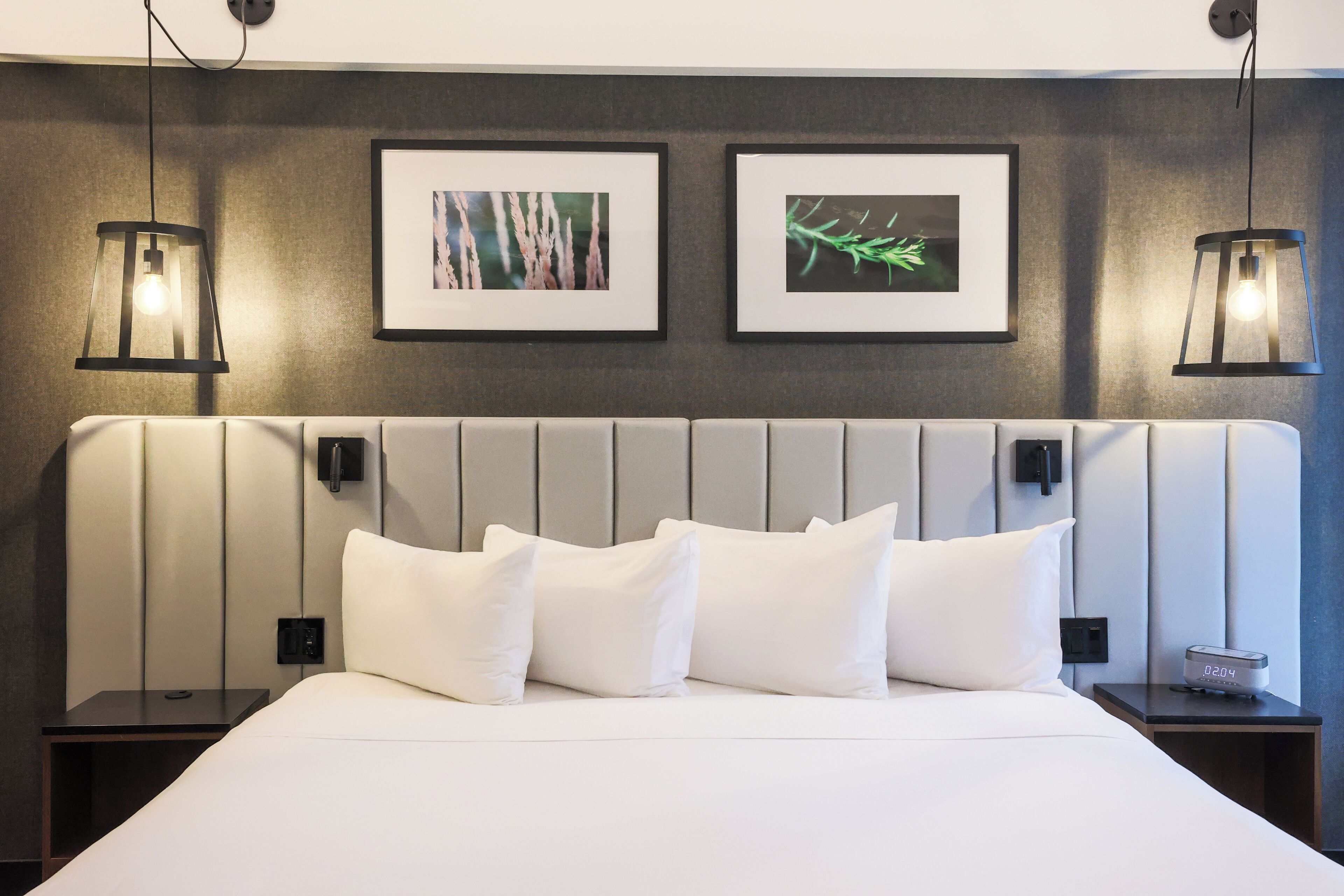 A neatly made bed with white linens and pillows, a modern headboard, and two wall-mounted picture frames.