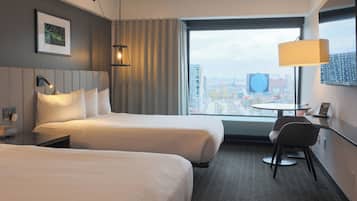 Une chambre d’hôtel avec deux lits, un bureau, une chaise et une grande fenêtre donnant sur la ville.