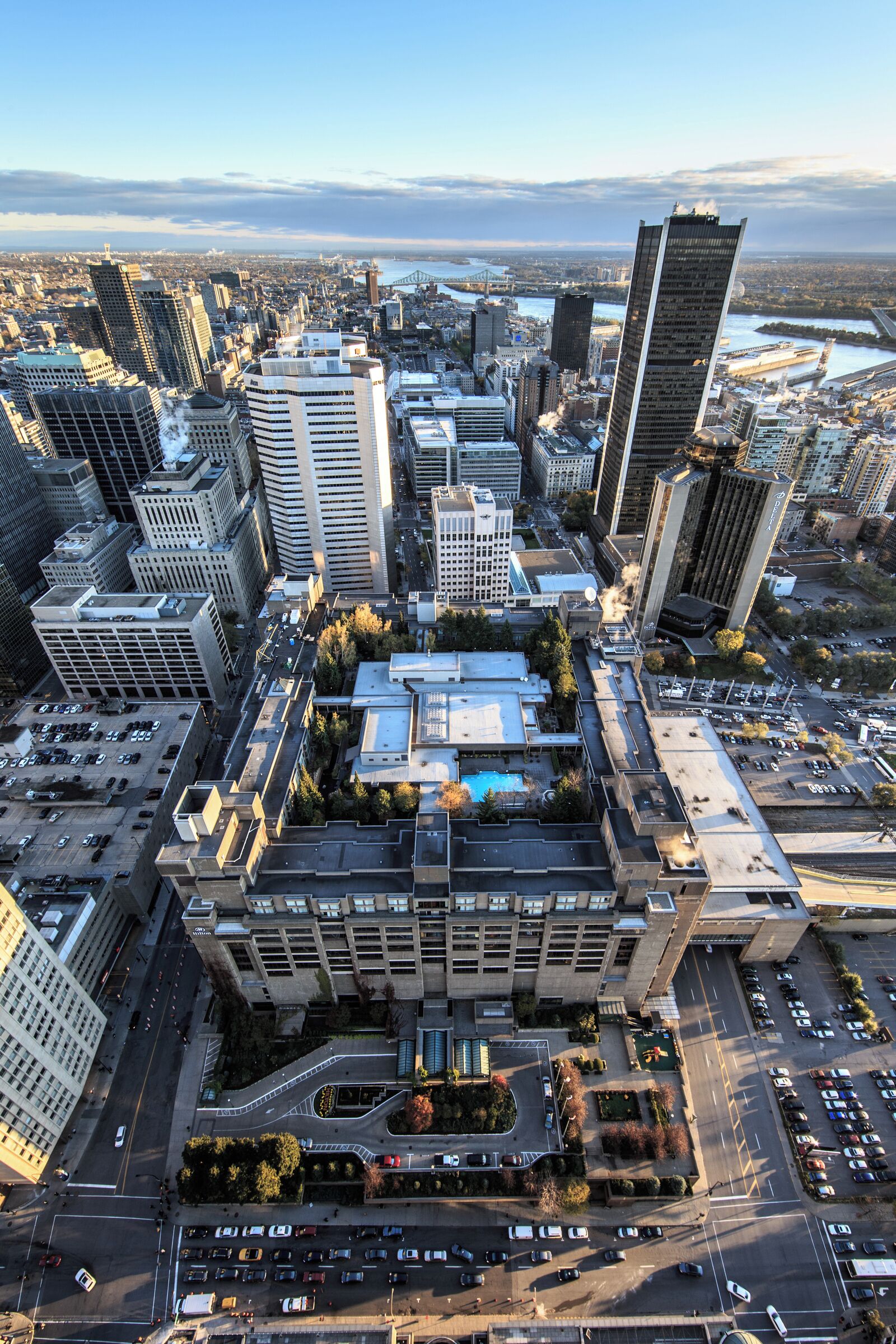 An aerial view of a cityscape with a prominent building featuring a rooftop garden and a parking lot.
