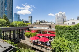 Un restaurante en la azotea con mesas al aire libre y sombrillas rojas, con vistas a un paisaje urbano de edificios modernos.