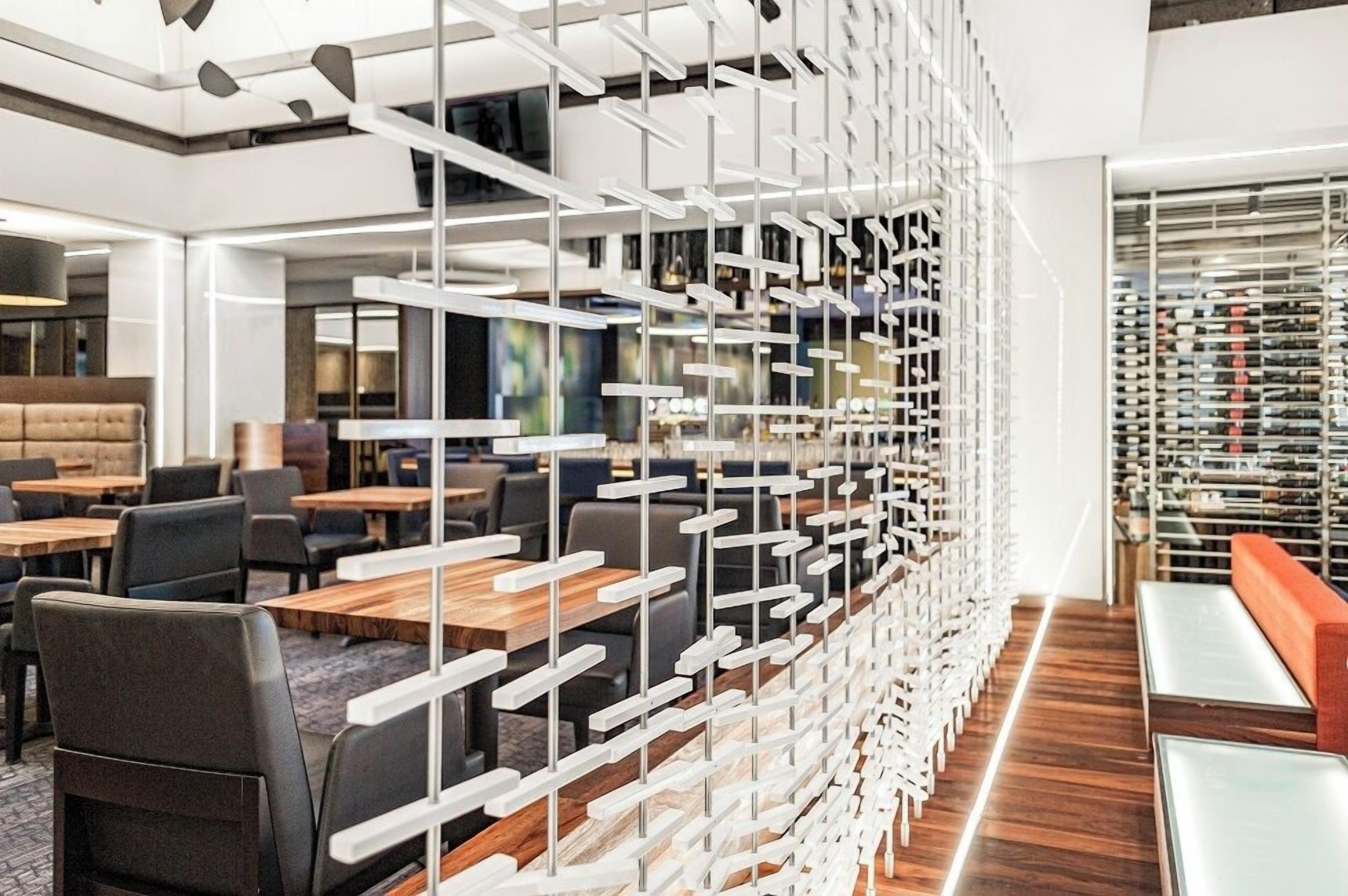 A modern interior with a wooden floor, black and gray chairs, and tables. There is a white partition with a geometric design.