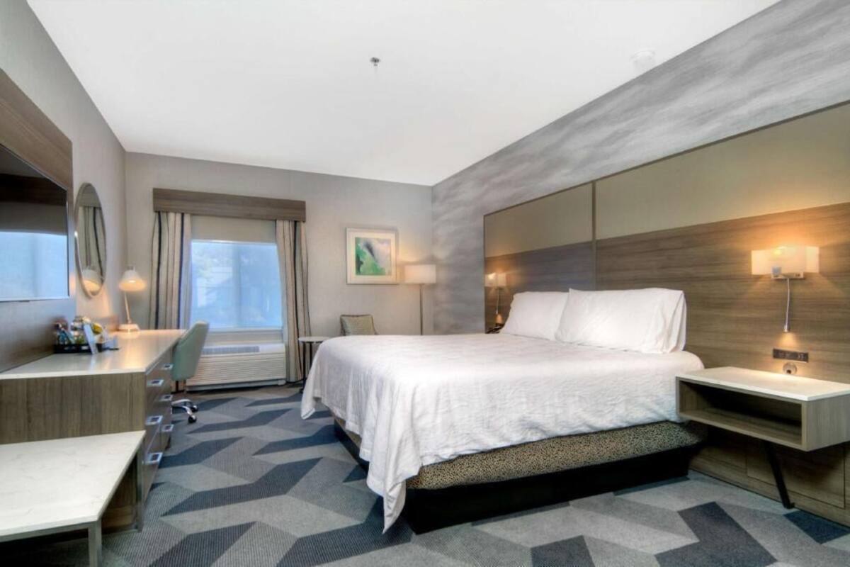 Habitación de hotel con cama, escritorio, silla y un gran ventanal.