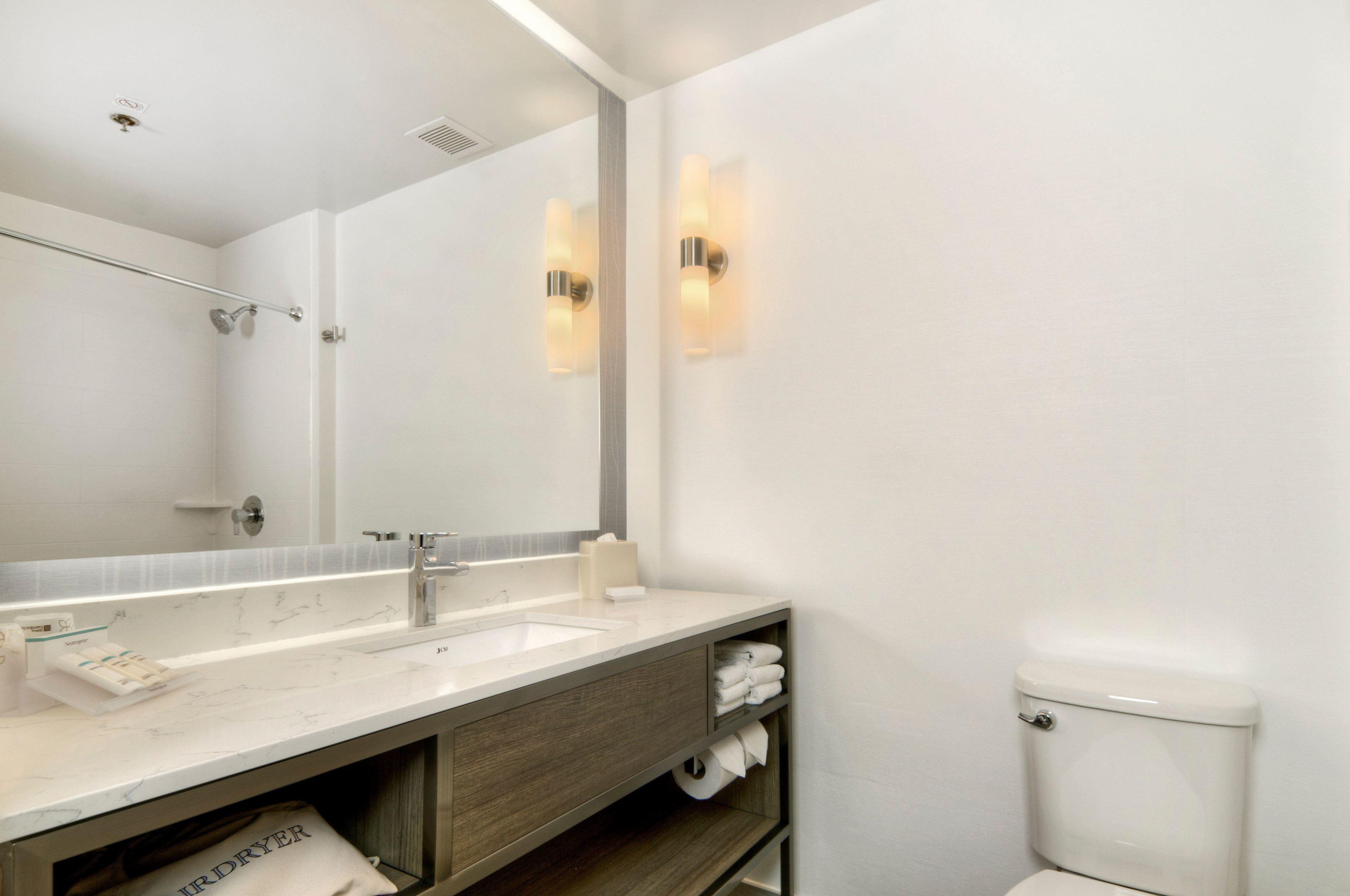 A modern bathroom with a large mirror, a sink, a toilet, and a towel rack.