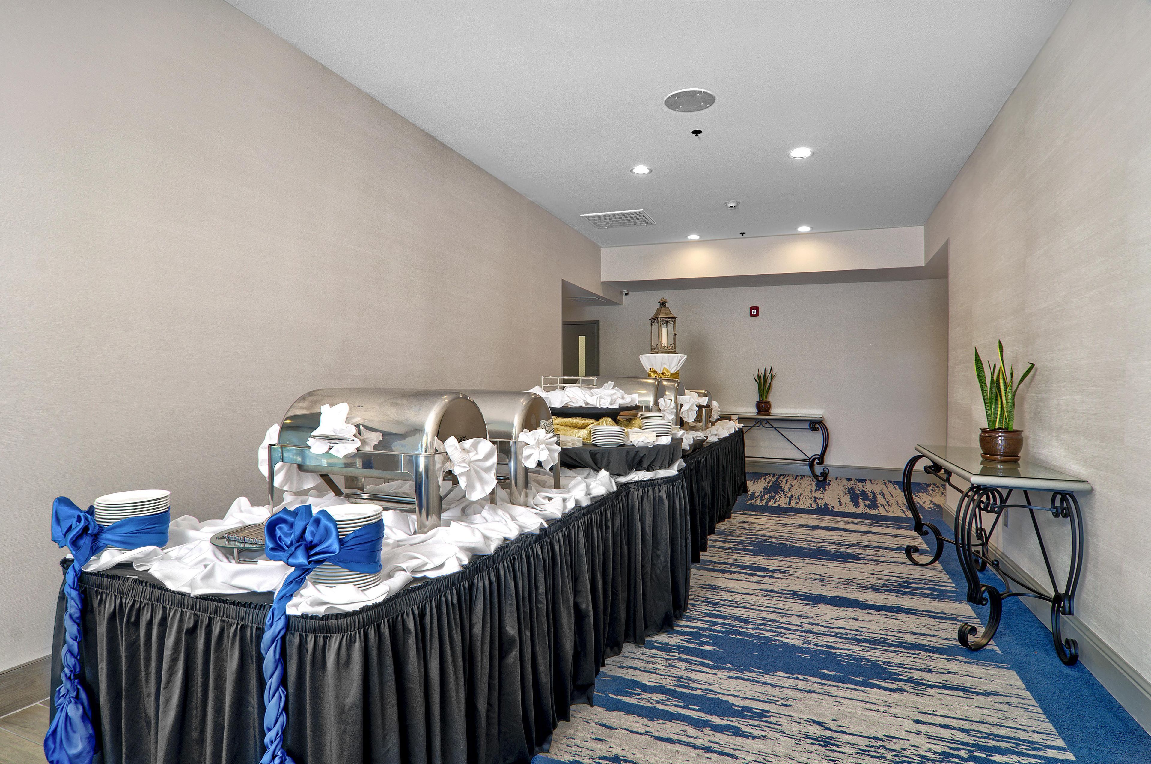 A buffet setup with a long table, covered with a black tablecloth and white napkins tied with blue ribbons.