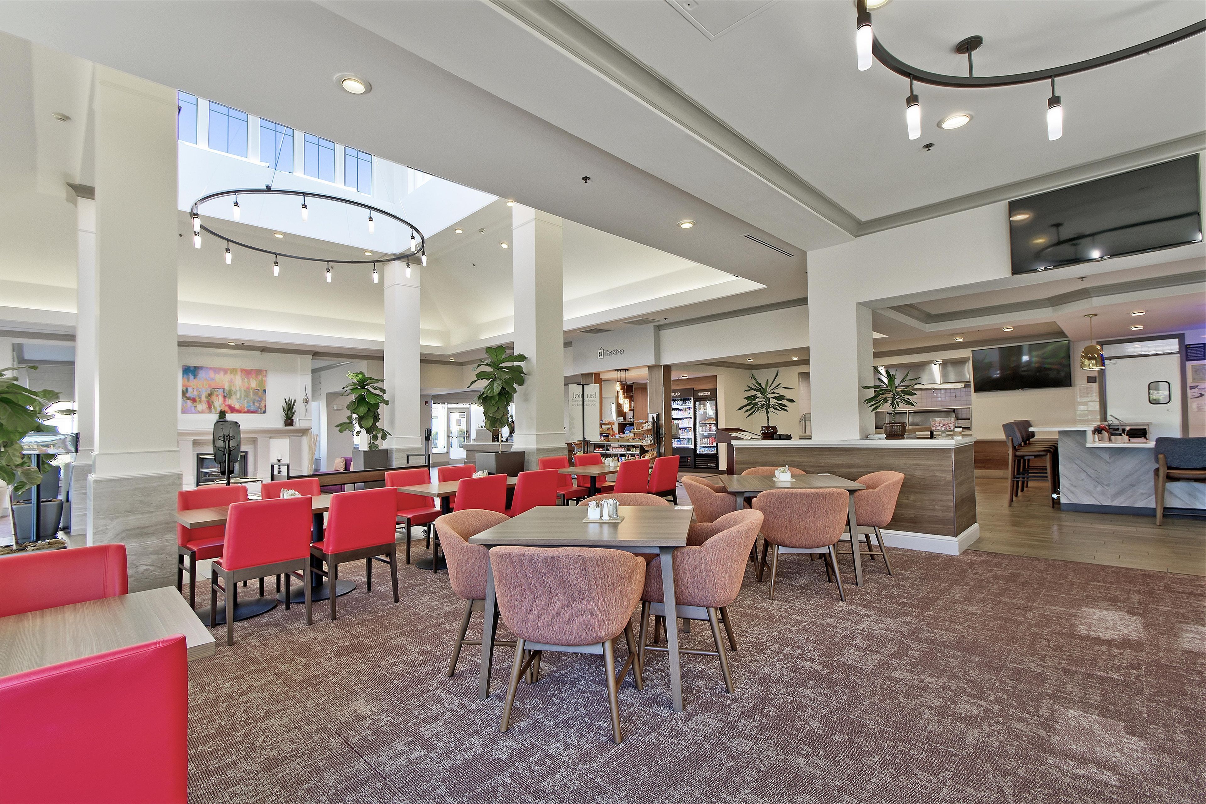A spacious hotel lobby with high ceilings, multiple seating areas, and a central island with a kitchen counter.