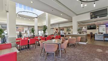 A spacious hotel lobby with high ceilings, multiple seating areas, and a central island with a kitchen counter.