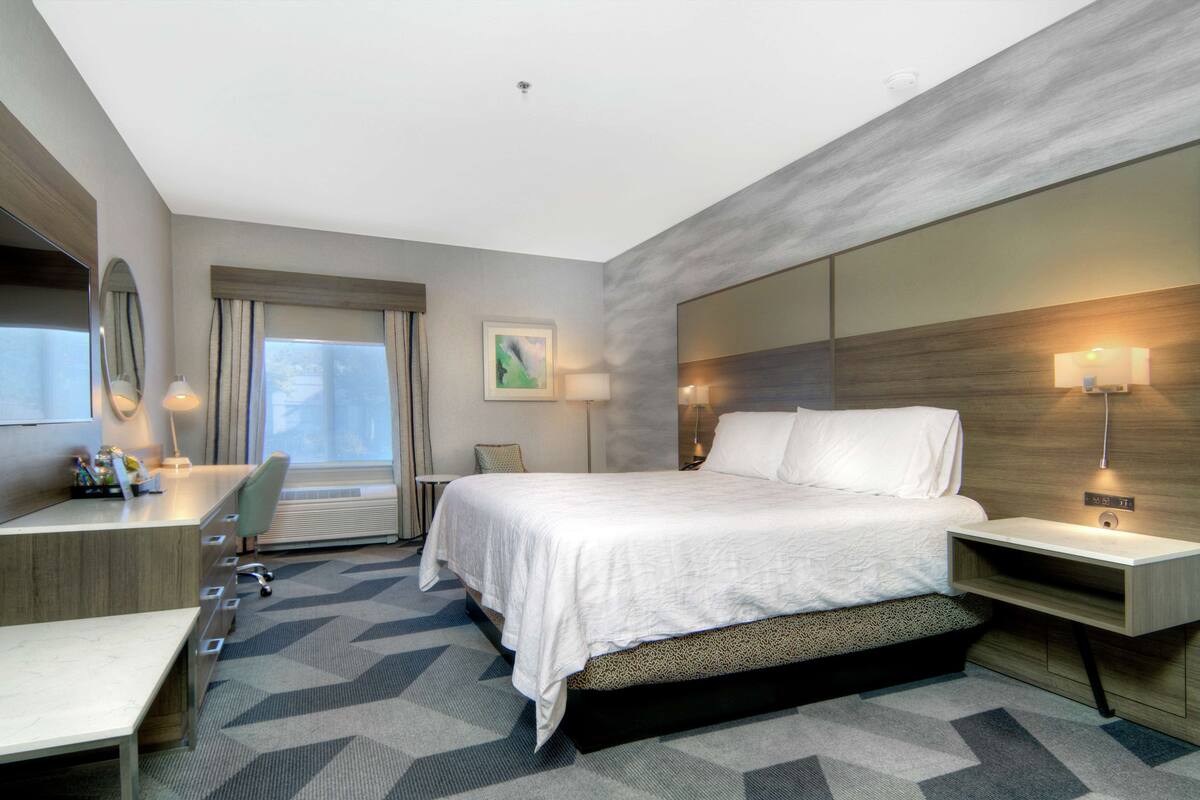 Una habitación de hotel moderna con una cama grande, un escritorio, una silla y una lámpara de escritorio.