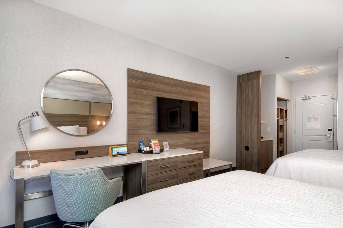 Habitación de hotel con cama, escritorio y silla, televisor montado en la pared y puerta.