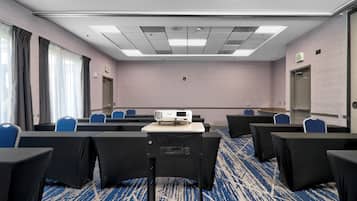 A conference room with a projector, rows of chairs, an exit sign, and a carpeted floor.