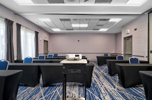 Un salón de conferencias con proyector, hileras de sillas, señal de salida y piso alfombrado.