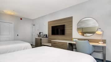 Habitación de hotel con dos camas, un escritorio con silla, televisor, espejo y una kitchenette pequeña.