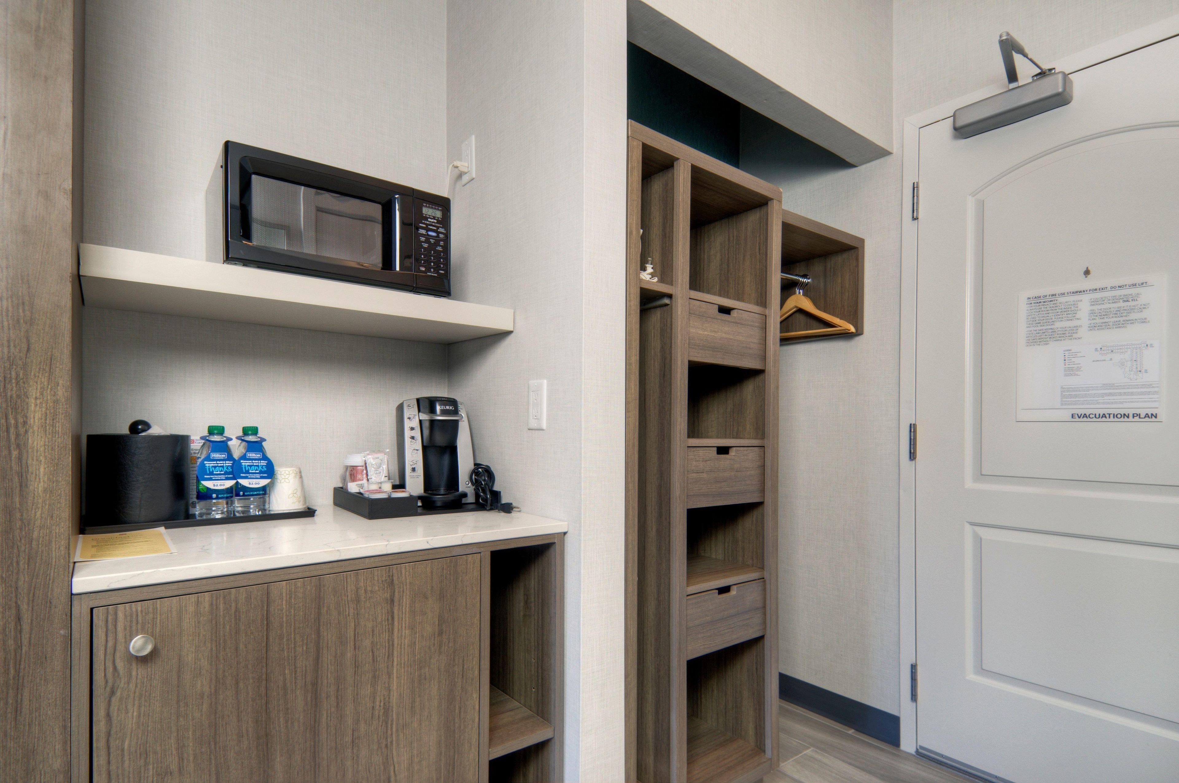 A kitchenette with a microwave, coffee maker, and water bottles.