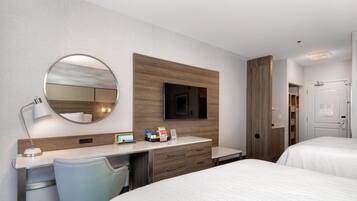 A hotel room with a bed, a desk with a chair, a TV, a mirror, and a door.