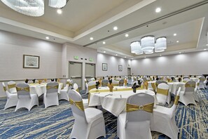 A banquet hall with round tables, chairs with gold sashes, and exit signs on the walls. - Hilton Garden Inn Livermore (Livermore)