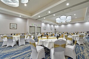 Un salón de banquetes con mesas redondas, sillas con cintas doradas y señales de salida en las paredes.