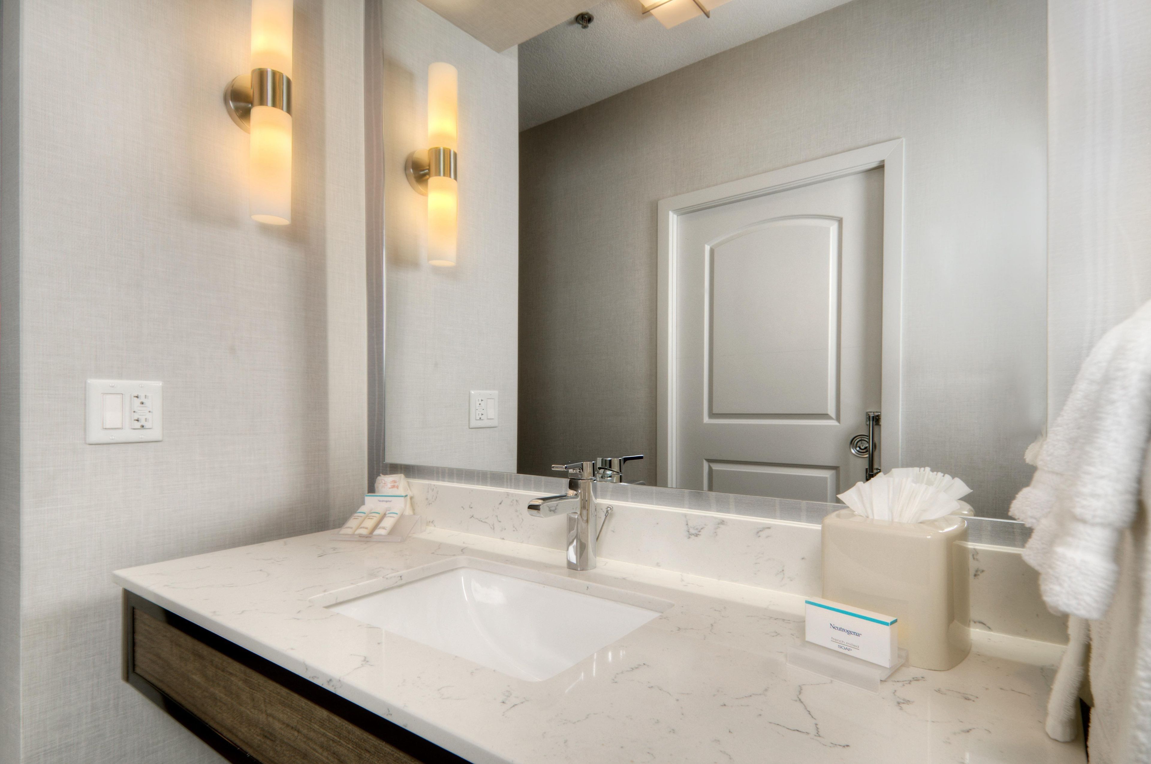 A modern bathroom with a marble countertop, a mirror, a towel dispenser, and a door.