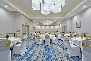 A conference room with round tables, white chairs with gold sashes, and a blue patterned carpet.