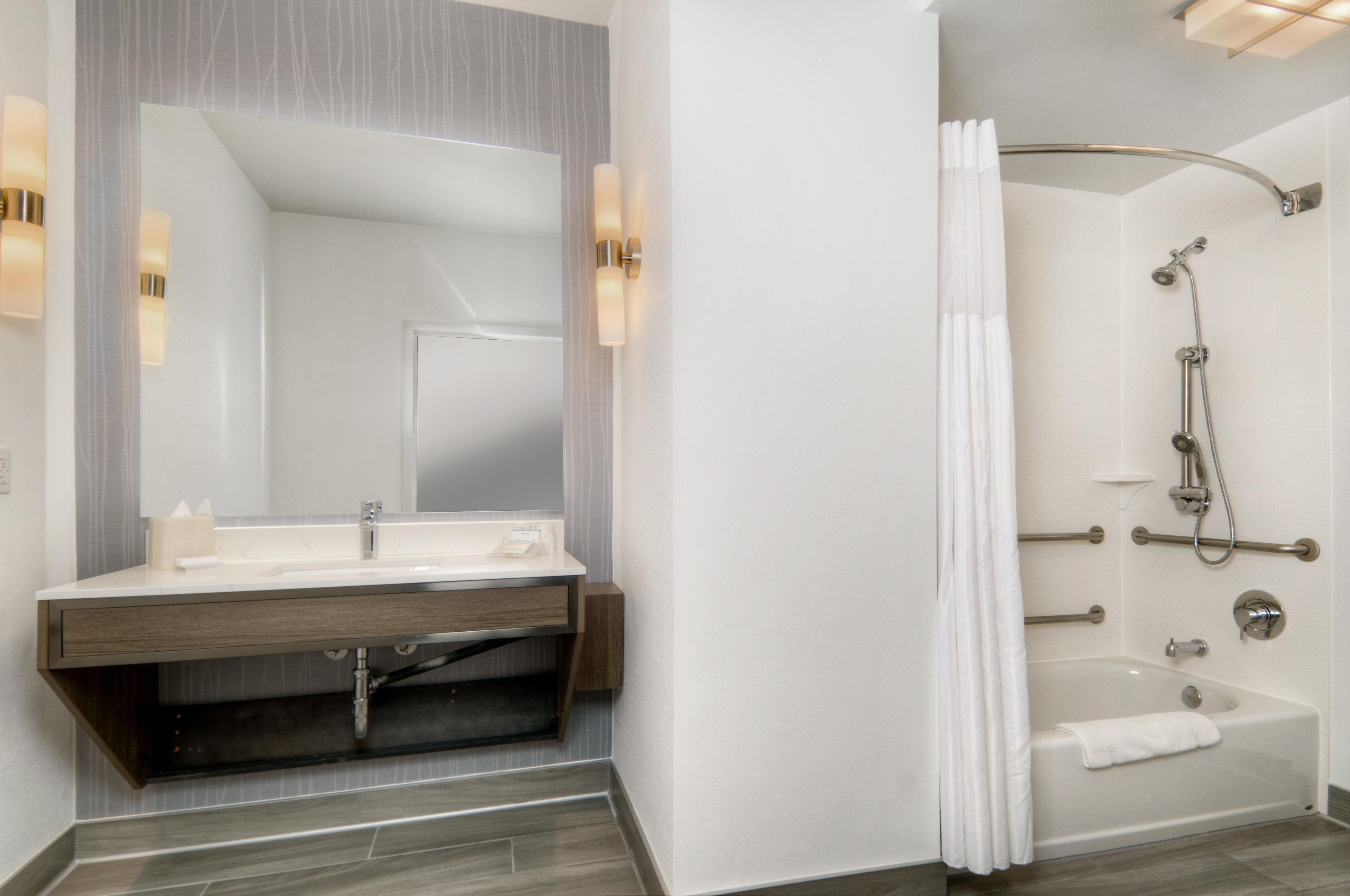 A modern bathroom with a vanity, mirror, shower, and bathtub.