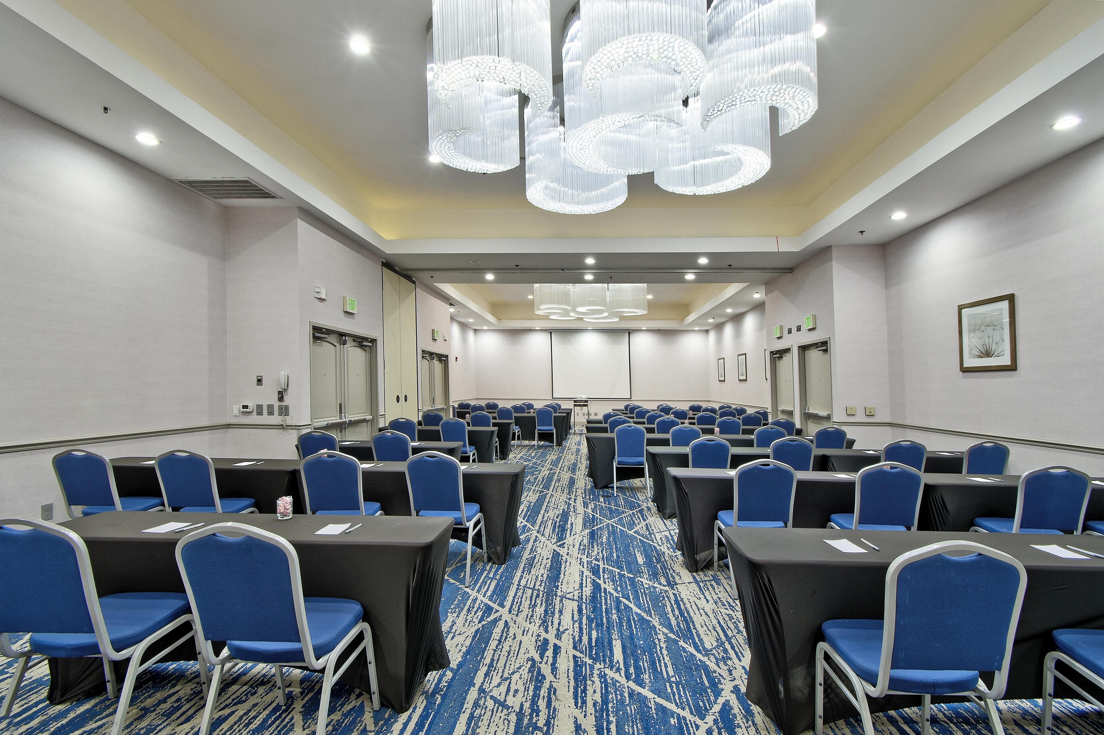 Une salle de conférence avec des rangées de tables et de chaises, une moquette à motifs et un lustre moderne.