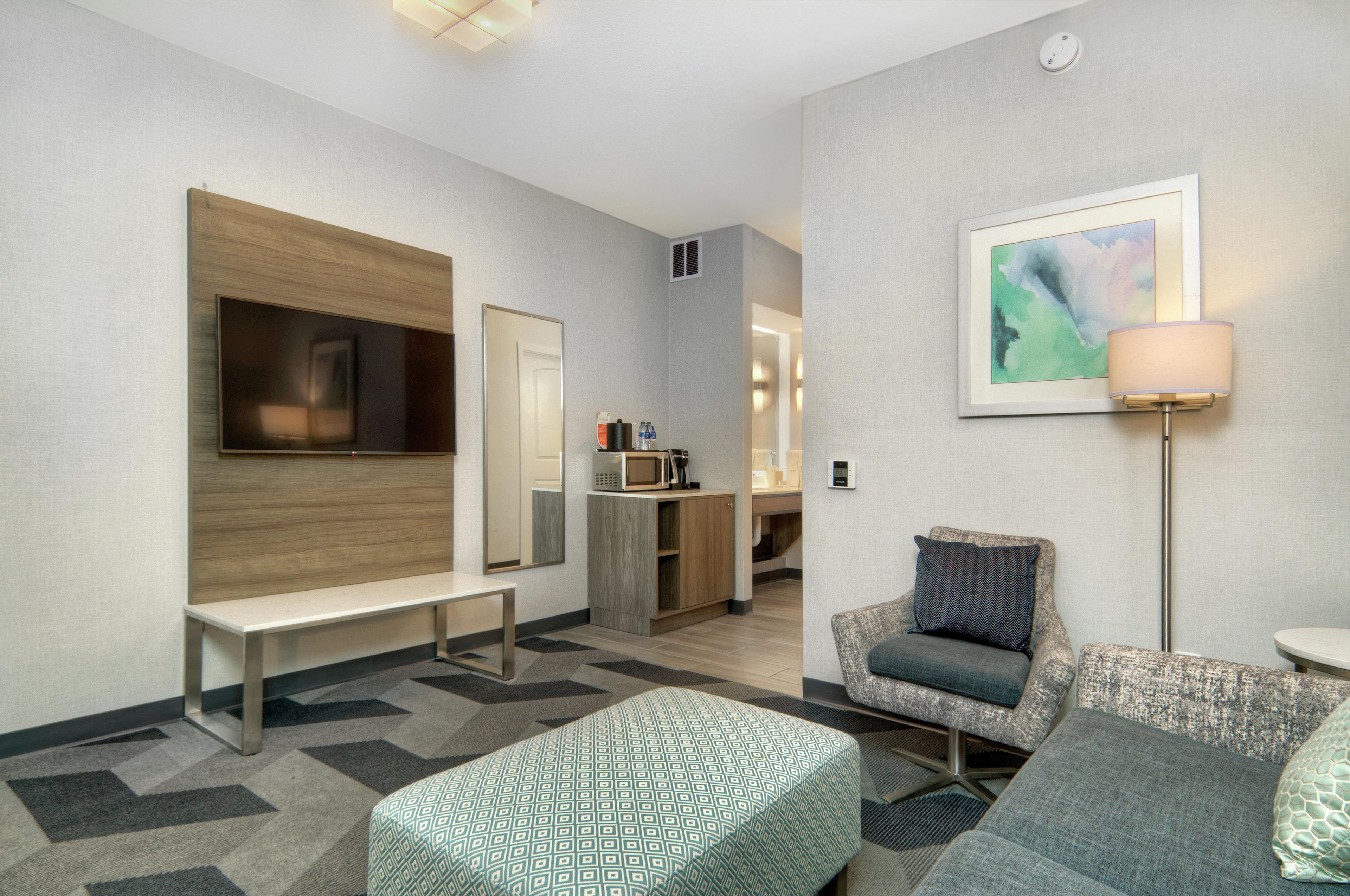 A hotel room with a TV, a bench, a sofa, a lamp, and a painting on the wall.
