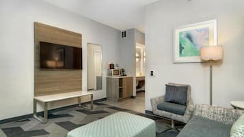 A hotel room with a TV, a bench, a sofa, a lamp, and a painting on the wall.