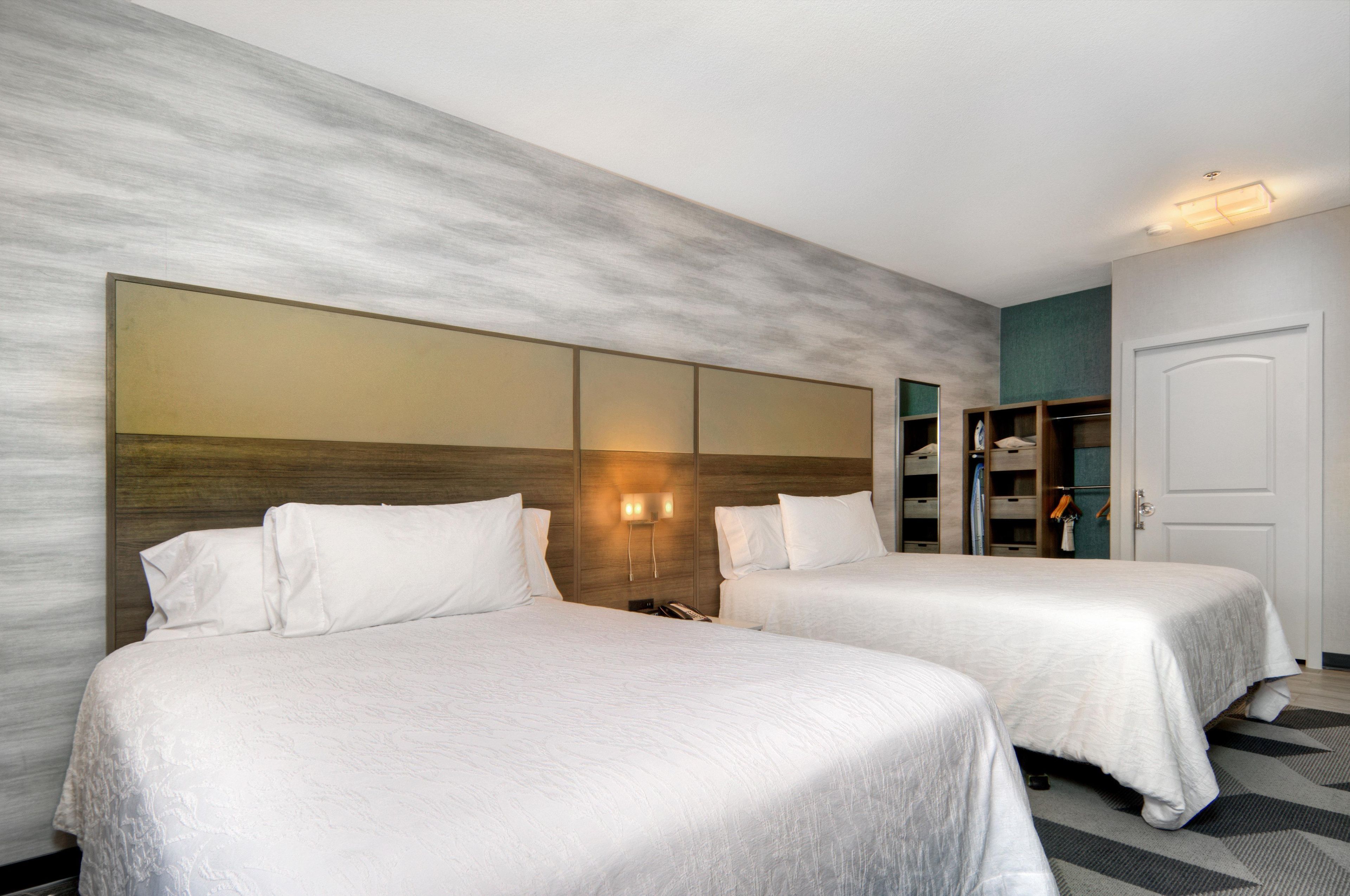 A hotel room with two beds, a wardrobe, and a mirror on the wall.