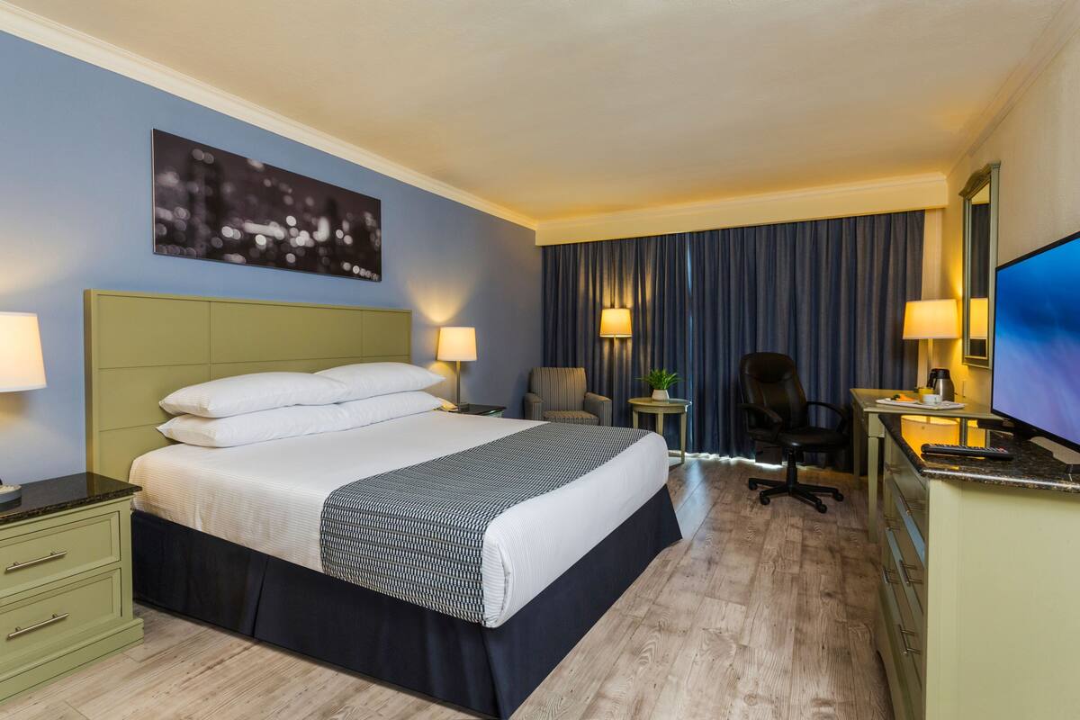 Et hotelværelse med en stor seng, et skrivebord med computer, en stol og et fjernsyn.