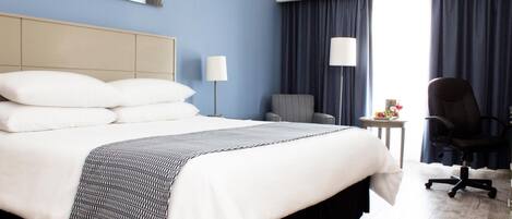 Una habitación de hotel con una cama grande, una silla, un escritorio y una lámpara.