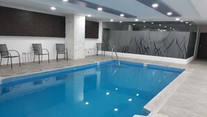 An indoor swimming pool with a clear blue water, surrounded by chairs and a wall with abstract designs. - Krystal Urban Ciudad Juárez by US Consulate (Ciudad Juárez)