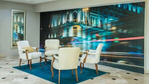 A lobby with a large digital mural of a cityscape, a blue carpet, and four upholstered chairs with wooden legs. - Krystal Urban Ciudad Juárez by US Consulate (Ciudad Juárez)