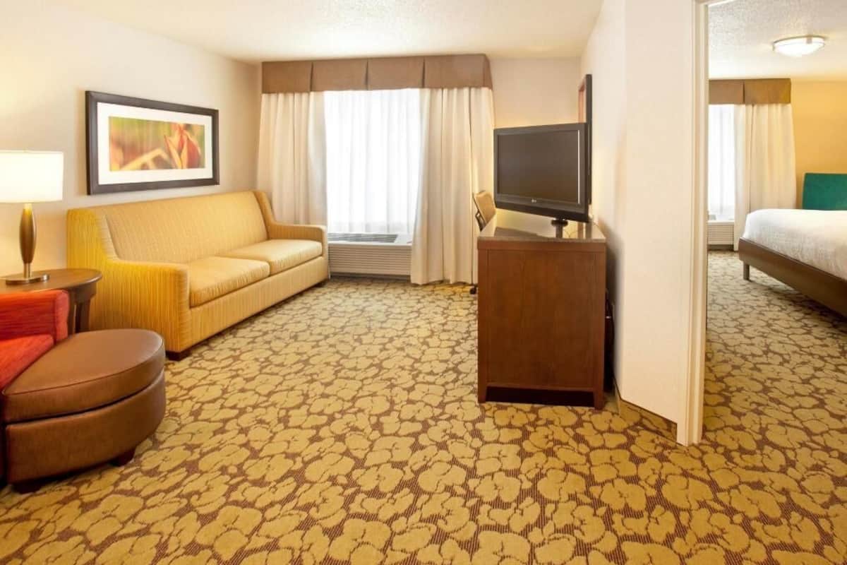 Een hotelkamer met een bank, een televisie op een houten standaard, een kamerbreed tapijt met dessin en een bed.