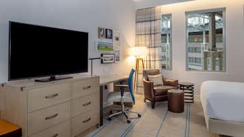 Une chambre d’hôtel équipée d’une télévision à écran plat, d’un bureau avec une chaise, d’un lit, d’une lampe et d’une fenêtre donnant sur des immeubles.