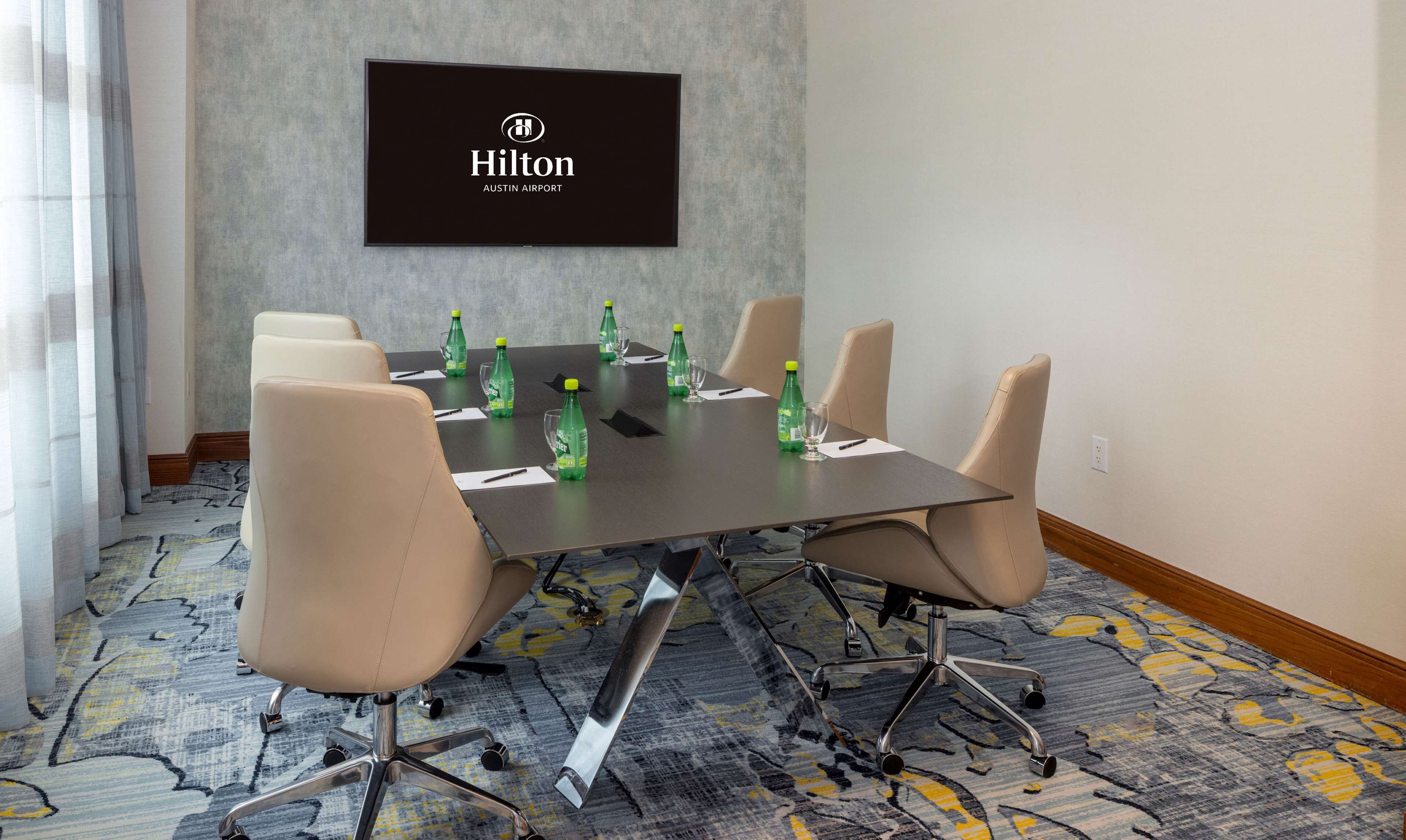 A conference room with a Hilton sign, a long table, six chairs, and water bottles on the table.