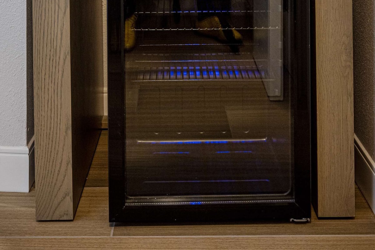 A compact kitchen area with a built-in oven, a wooden countertop, and a shelf above holding water bottles and a coffee maker.