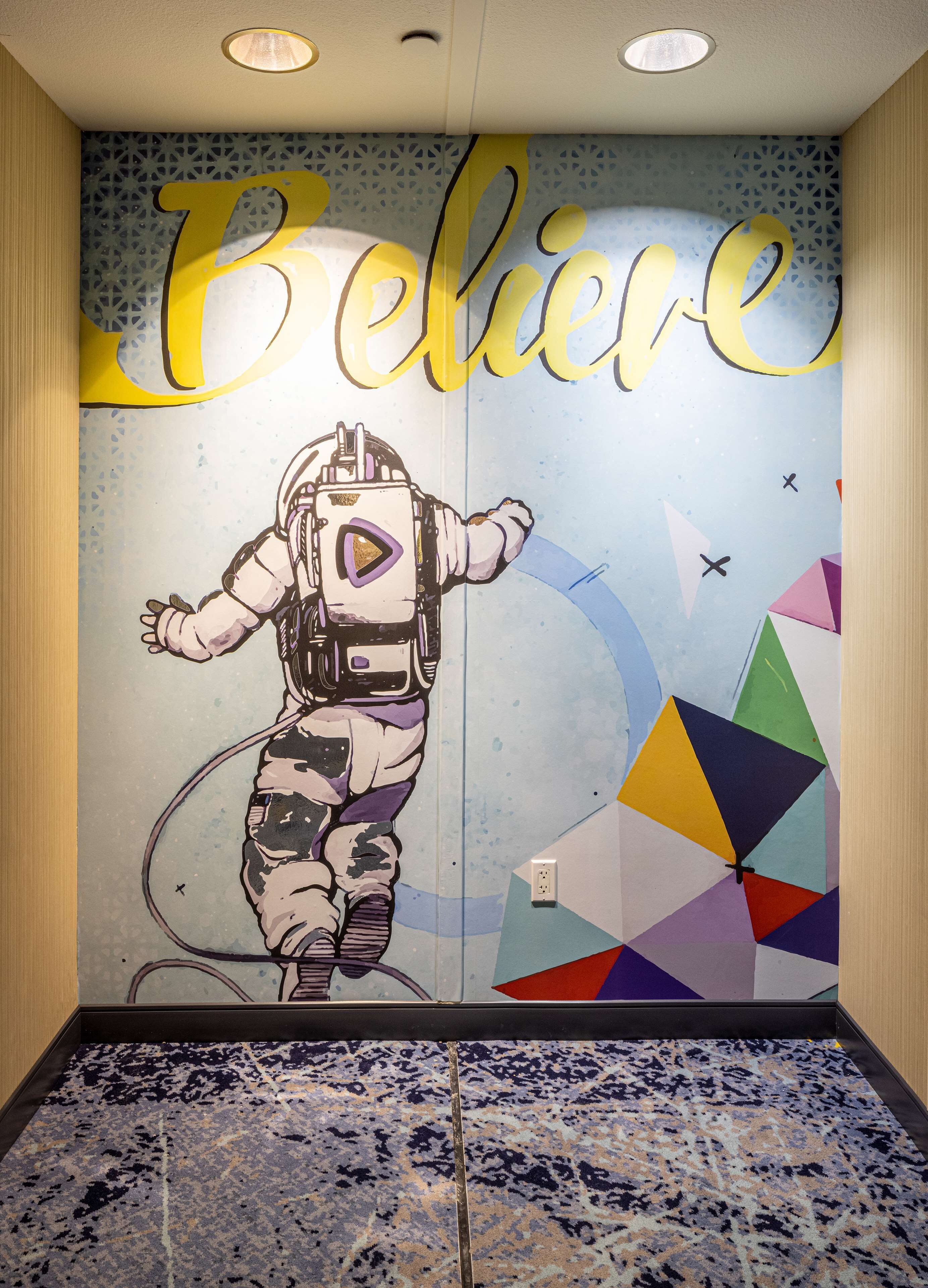A wall with a mural of an astronaut and the word "Believe" in large letters.