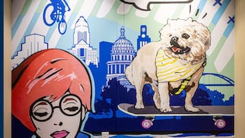 Un mural con un perro y una persona en un monopatín, una burbuja de diálogo que dice "¡ME ENCANTA ESTA CIUDAD!", y un paisaje urbano al fondo.