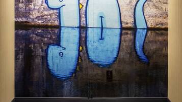 A wall with graffiti of a blue dinosaur and a reflection of the same on the floor.